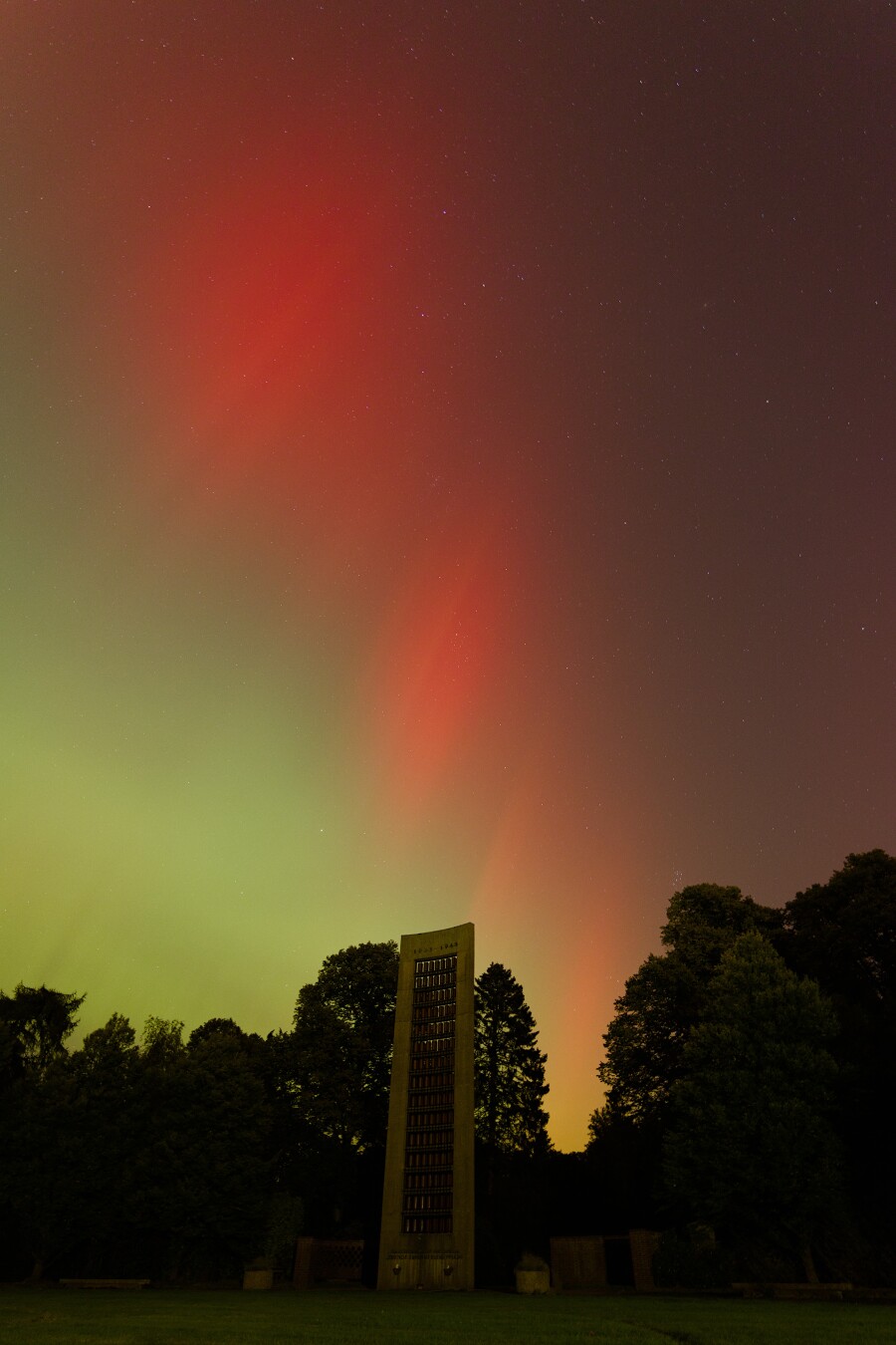 DE: Rote und leicht grüne Polarlichter am Himmel über dem Mahnmal für die Opfer von nationalsozialistischer Verfolgung auf dem Ohlsdorfer Friedhof.

EN: Red and slightly green auroras in the sky above the memorial to the victims of National Socialist persecution at Ohlsdorf cemetery.